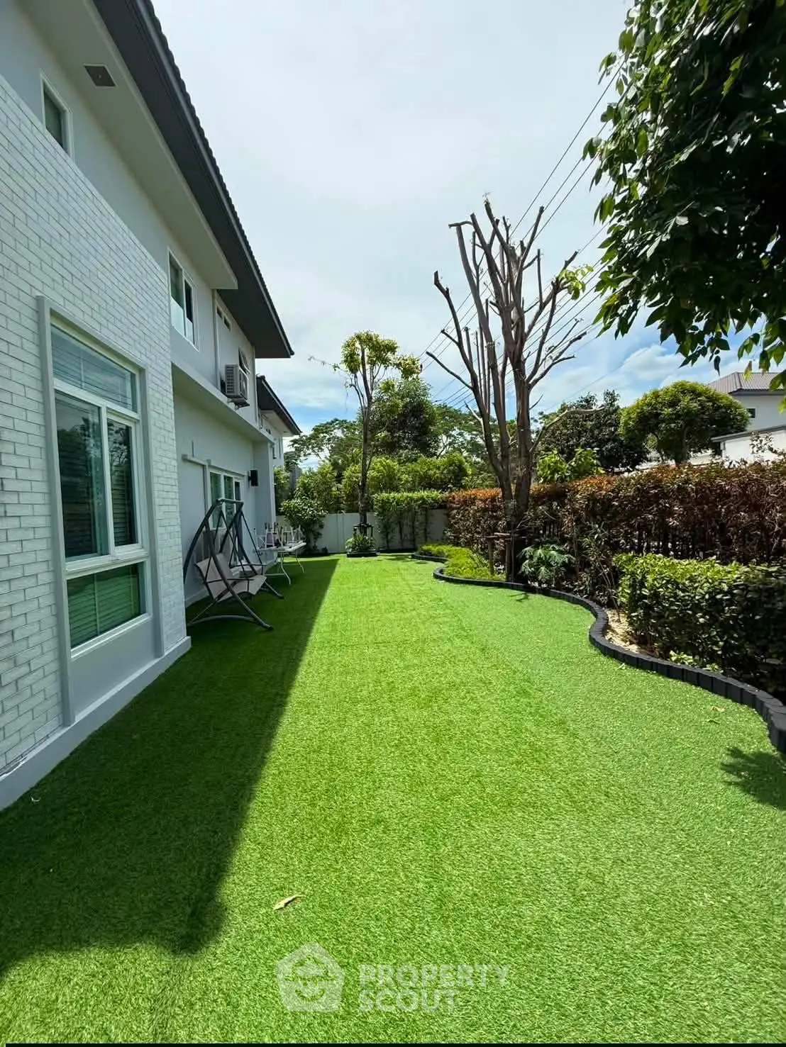 Charming backyard with lush artificial grass and modern white brick house exterior.