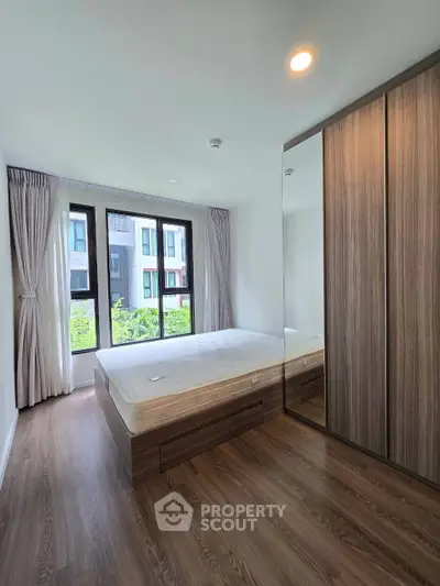 Spacious bedroom with large window and built-in wardrobe in modern apartment.