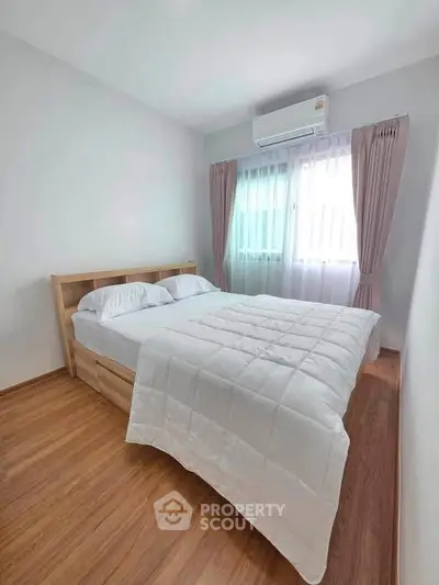 Cozy bedroom with wooden flooring and natural light, featuring a comfortable bed and air conditioning.