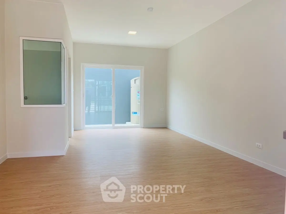 Spacious empty room with wooden flooring and large window for natural light.