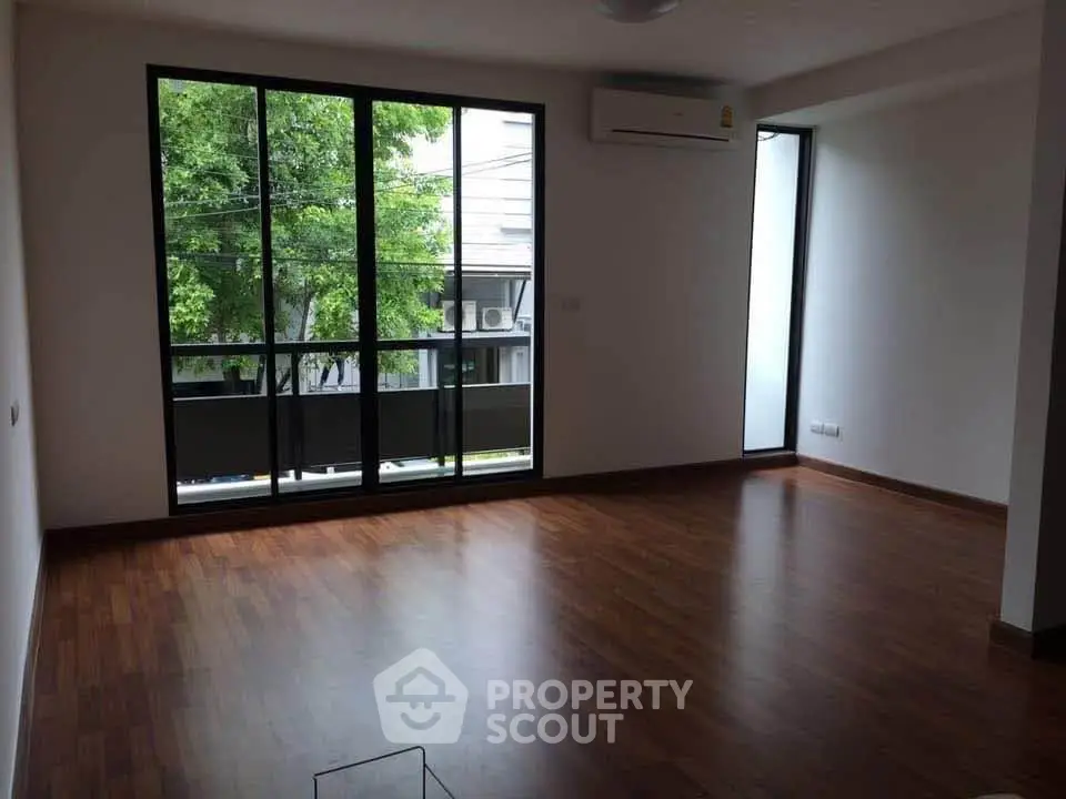 Spacious living room with large windows and wooden flooring, offering natural light and a serene view.