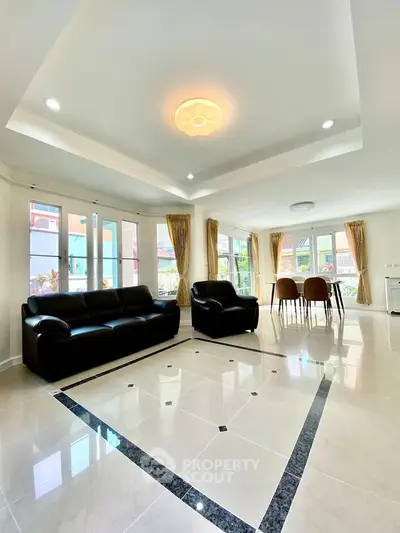 Spacious living room with modern black sofas and elegant dining area, featuring large windows and stylish lighting.