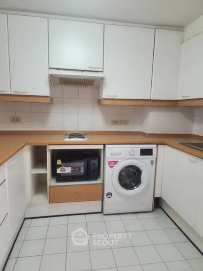 Modern kitchen with washing machine and microwave, featuring sleek white cabinets and tiled flooring.