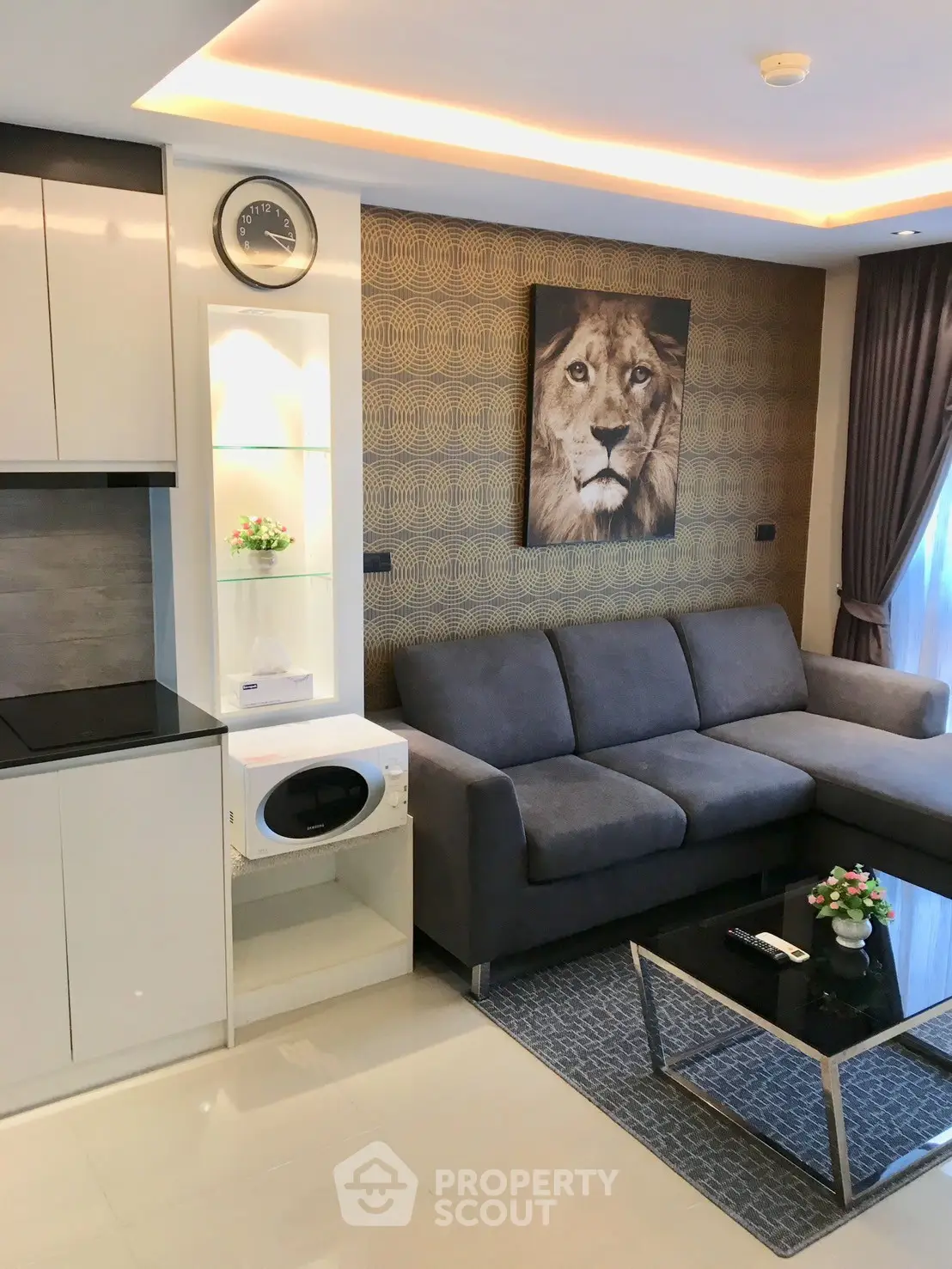 Modern living room with sleek design, featuring a gray sofa, lion artwork, and stylish kitchen area.