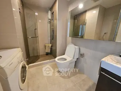 Modern bathroom with shower, washing machine, and sleek fixtures.