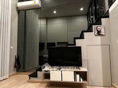 Modern living room with sleek staircase and wall-mounted TV, featuring stylish decor and air conditioning.