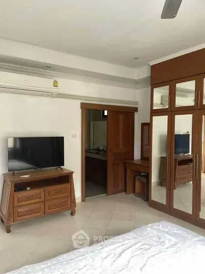 Spacious bedroom with wooden furniture and mirrored wardrobe, featuring a TV and air conditioning.