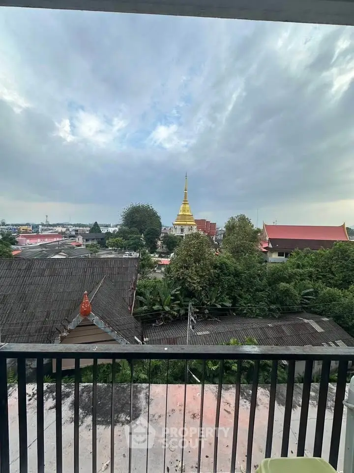 Stunning balcony view overlooking lush greenery and a golden temple spire.
