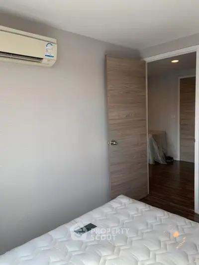 Modern bedroom with air conditioning and wooden flooring, featuring a comfortable mattress and open door.