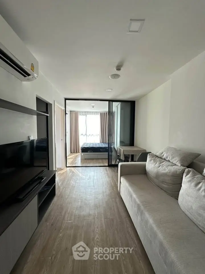 Modern living room with sleek design and open view to bedroom, featuring a cozy sofa and entertainment unit.