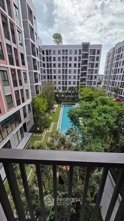 Modern apartment complex with pool view from balcony, lush greenery and stylish architecture.