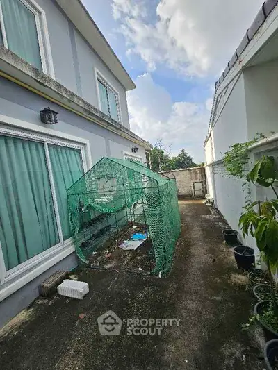 Charming backyard with greenhouse beside modern two-story home under blue sky.