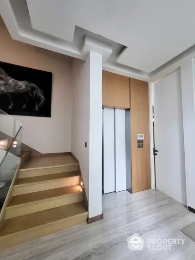 Modern home entrance with elegant staircase and sleek white doors, complemented by warm lighting and a sophisticated art piece.