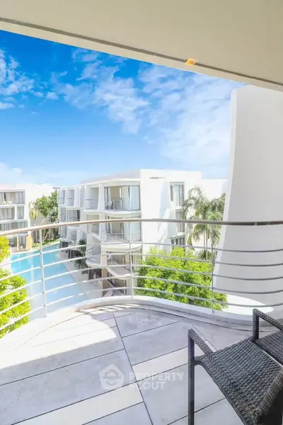 Stunning balcony view overlooking modern apartment complex with lush greenery and clear blue sky.