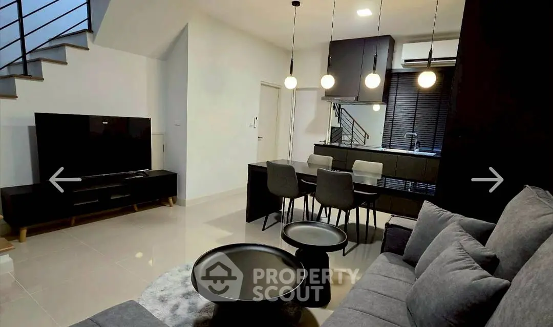 Modern living room with sleek furniture and open kitchen layout, featuring stylish lighting and contemporary design.