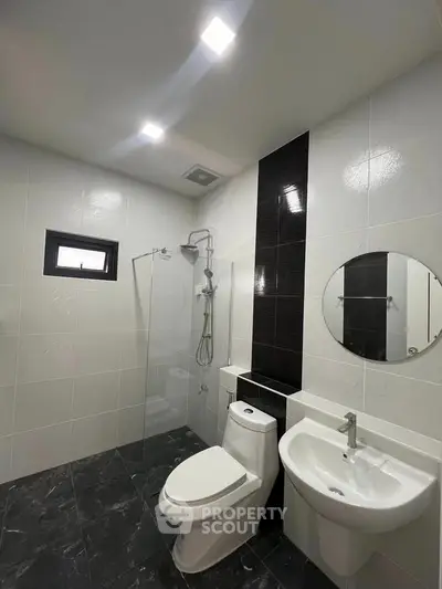 Modern bathroom with sleek black and white tiles, featuring a glass shower and contemporary fixtures.