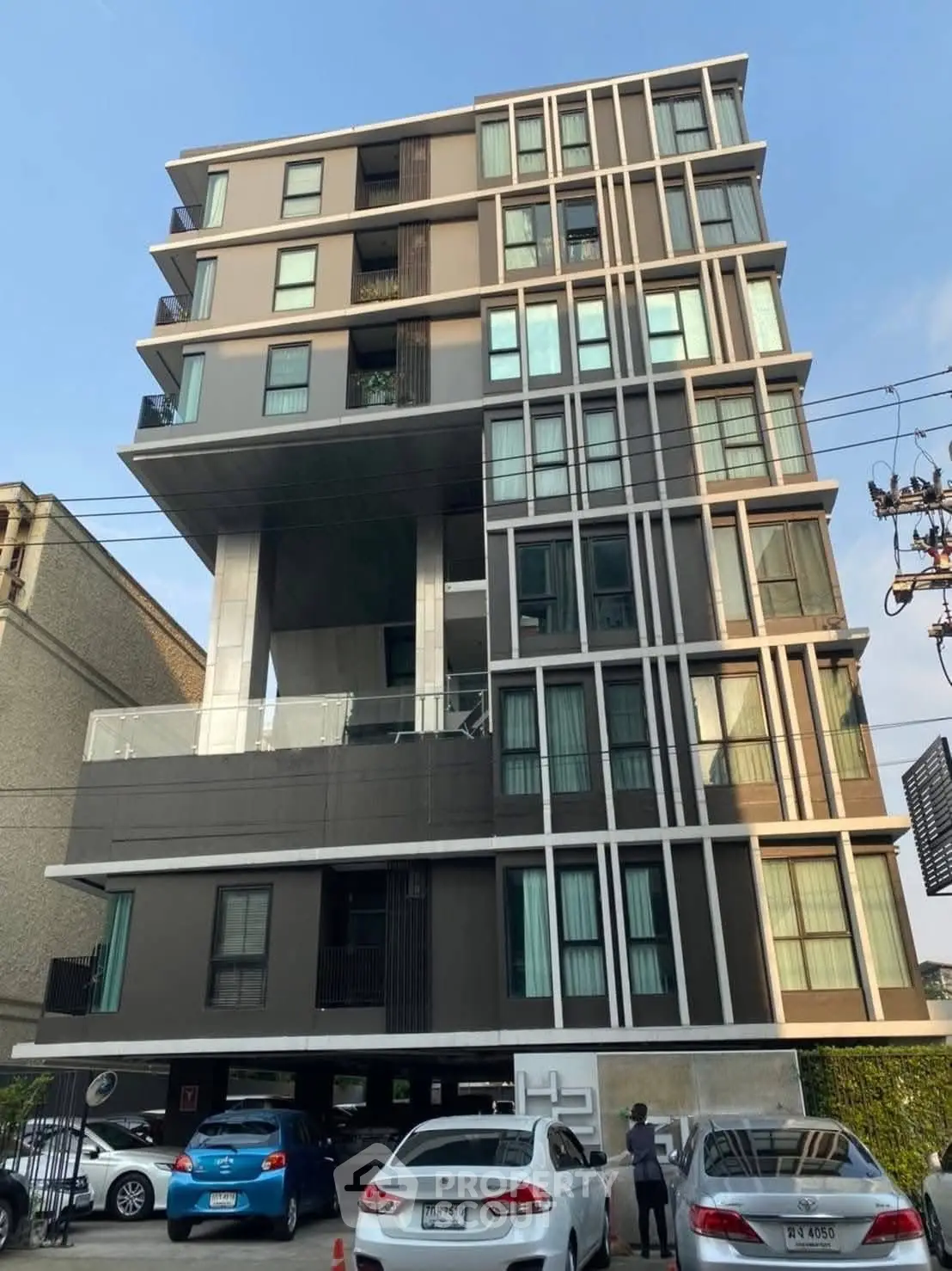 Modern multi-story apartment building with unique architectural design and ample parking space.