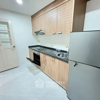 Modern kitchen with sleek wooden cabinets and stainless steel appliances in a compact layout.