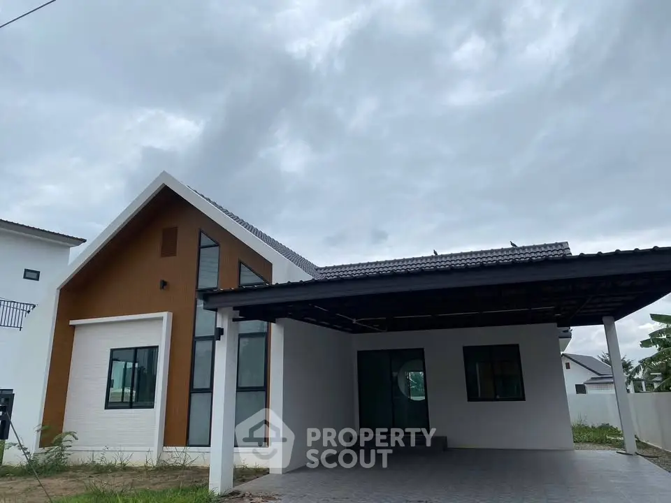 Modern minimalist house exterior with sleek design and spacious carport under cloudy sky.