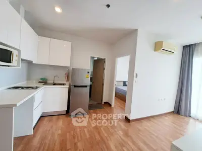 Modern open-layout kitchen with sleek white cabinets and hardwood floors in a bright apartment.