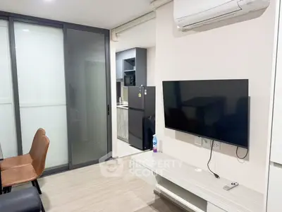 Modern living room with sleek design, featuring a wall-mounted TV and air conditioning, adjacent to a compact kitchen.