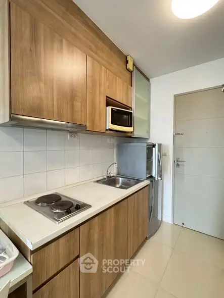 Modern compact kitchen with wooden cabinets and stainless steel appliances.