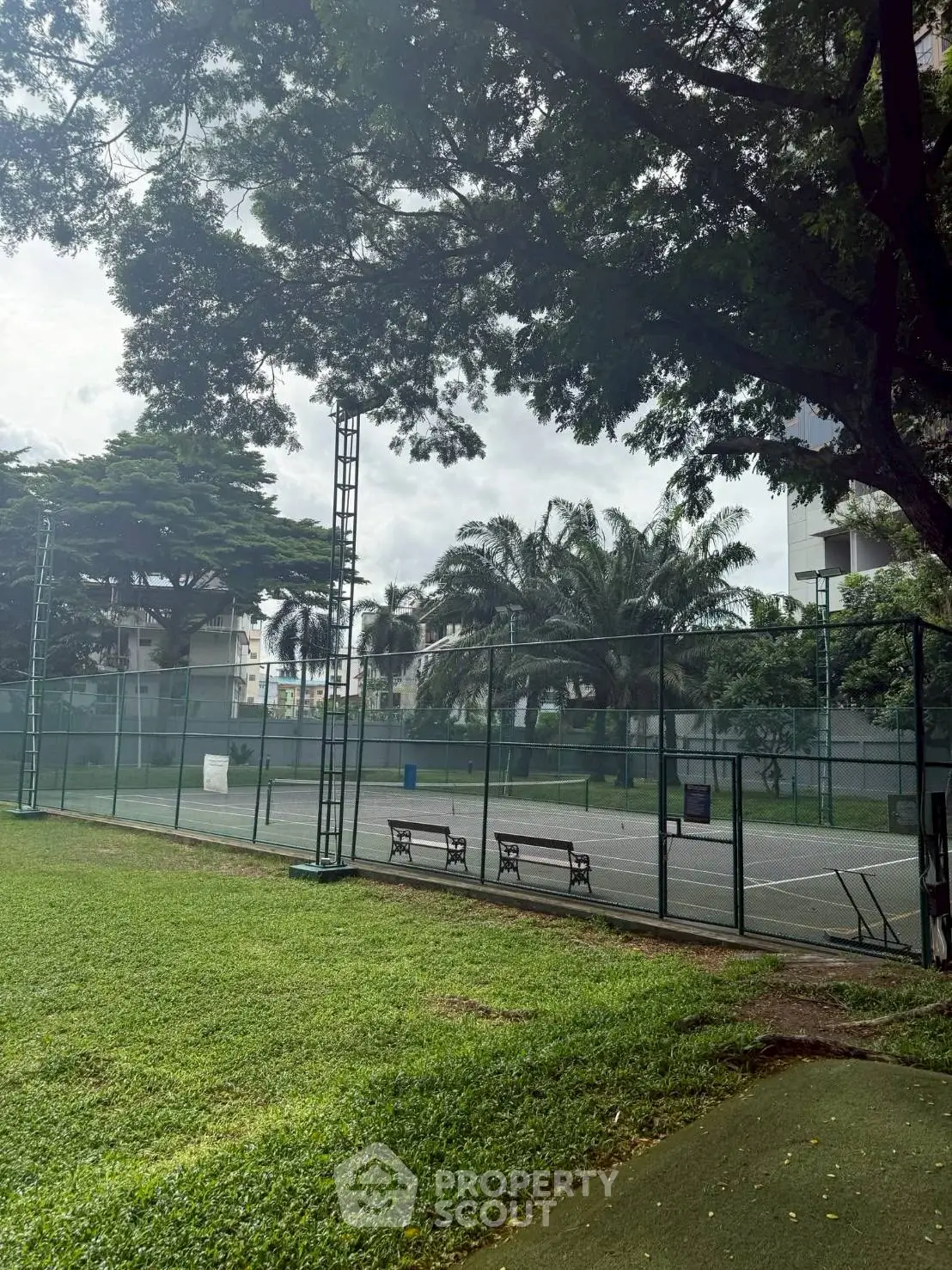 Spacious outdoor tennis court surrounded by lush greenery in a residential complex.