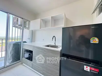 Modern kitchen with sleek cabinetry and balcony view, featuring a fridge and ample natural light.