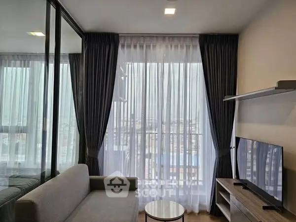 Modern living room with large windows and city view, featuring sleek furniture and elegant curtains.