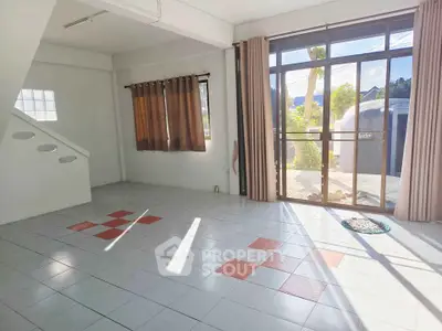 Spacious living room with large windows and tiled floor, offering abundant natural light and garden view.