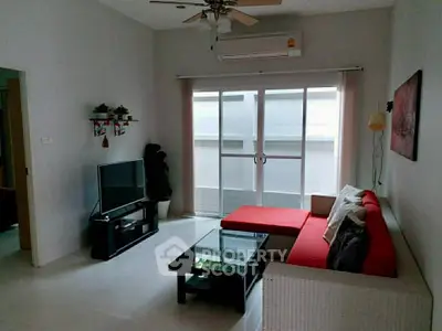 Modern living room with red sofa, glass coffee table, and large TV near balcony.