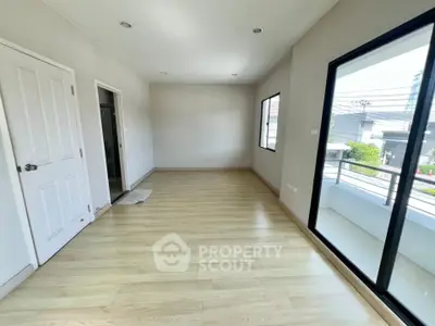 Spacious empty room with wooden flooring and balcony access in modern home