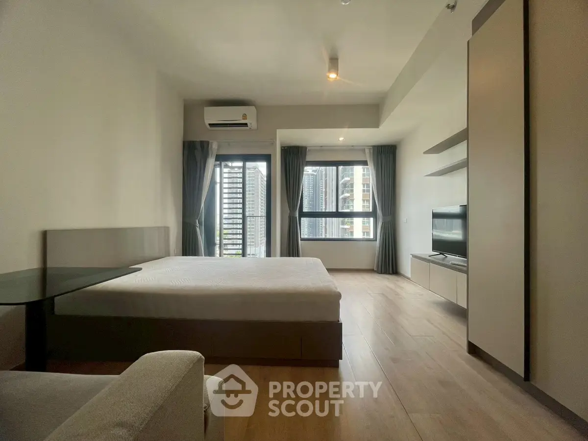 Spacious modern bedroom with large windows and city view, featuring sleek furniture and minimalist design.