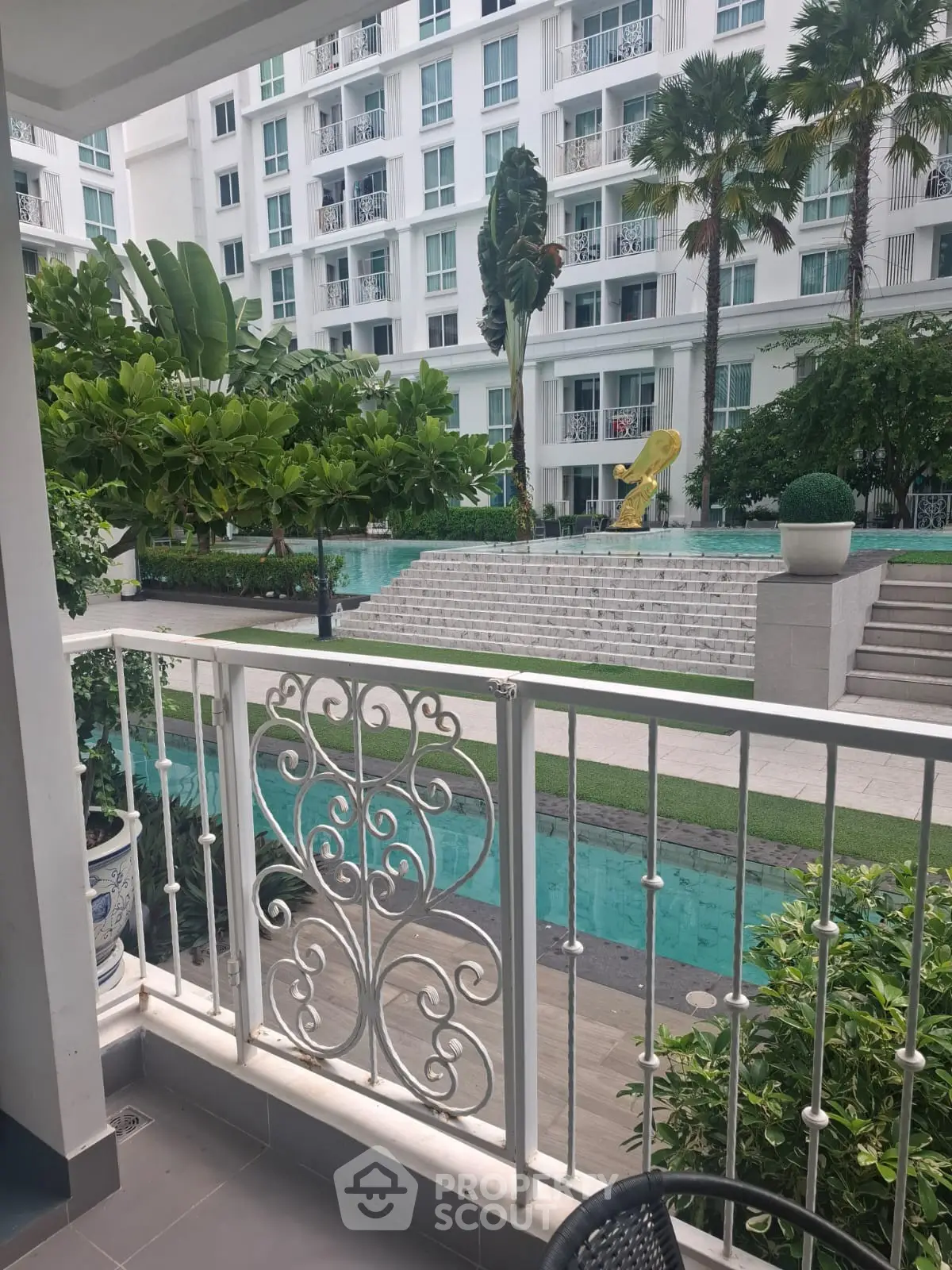 Luxurious apartment balcony overlooking a serene pool and lush garden in a modern residential complex.