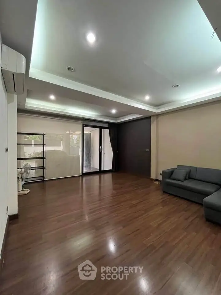 Spacious living room with modern lighting and hardwood floors, featuring a cozy sofa and large windows.