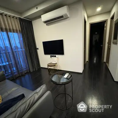 Modern living room with sleek dark hardwood floors, minimalist furniture, and a wall-mounted TV, complemented by soft curtains and ambient lighting.