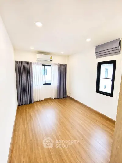 Spacious empty room with wooden flooring and large windows, perfect for customization.