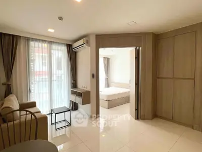 Modern living room with open view to bedroom, featuring sleek furniture and natural light.