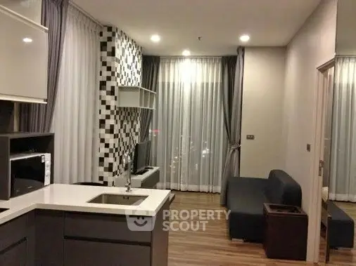 Modern open-layout living room with stylish kitchen and cozy seating area, featuring elegant wood flooring and chic decor.