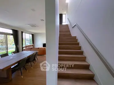 Spacious modern living room with dining area and staircase, featuring large windows and natural light.
