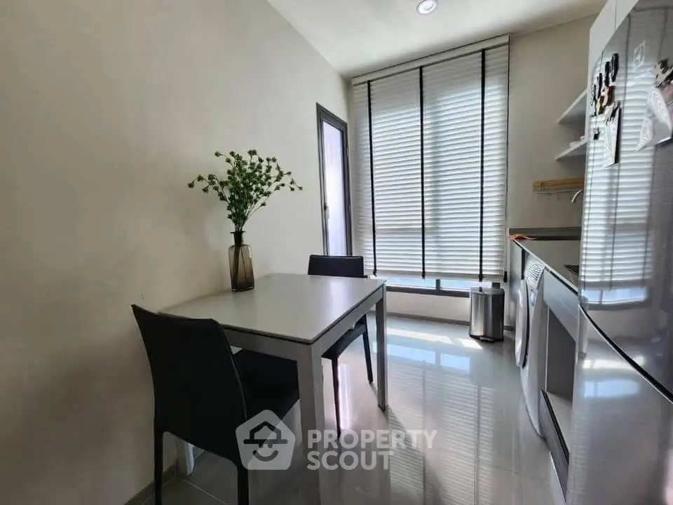Modern kitchen with sleek appliances and dining area, featuring natural light and contemporary design.