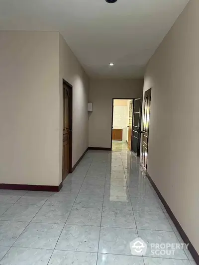 Spacious hallway in a residential property featuring gleaming marble floors, neutral walls, and multiple wooden doors leading to various rooms, ideal for family living.