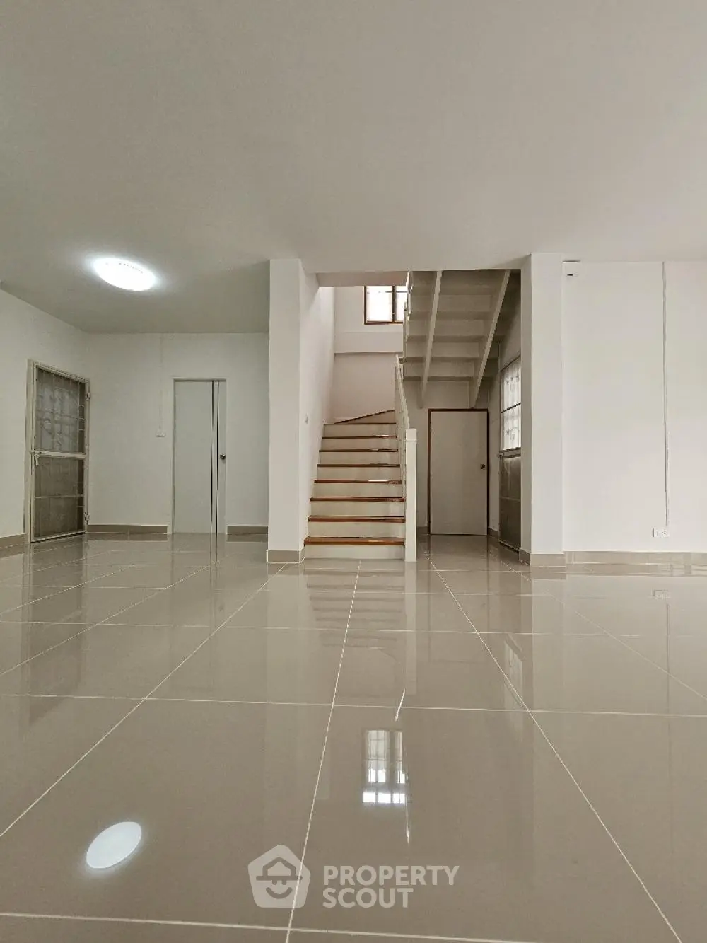 Spacious and bright open-plan living area with gleaming tiled floors, an elegant staircase leading to the upper level, and ample natural light from large windows, perfect for modern living.