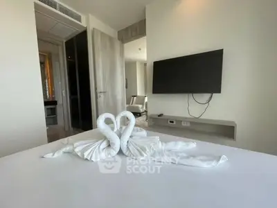 Elegant bedroom with swan towel decor and wall-mounted TV in modern apartment.