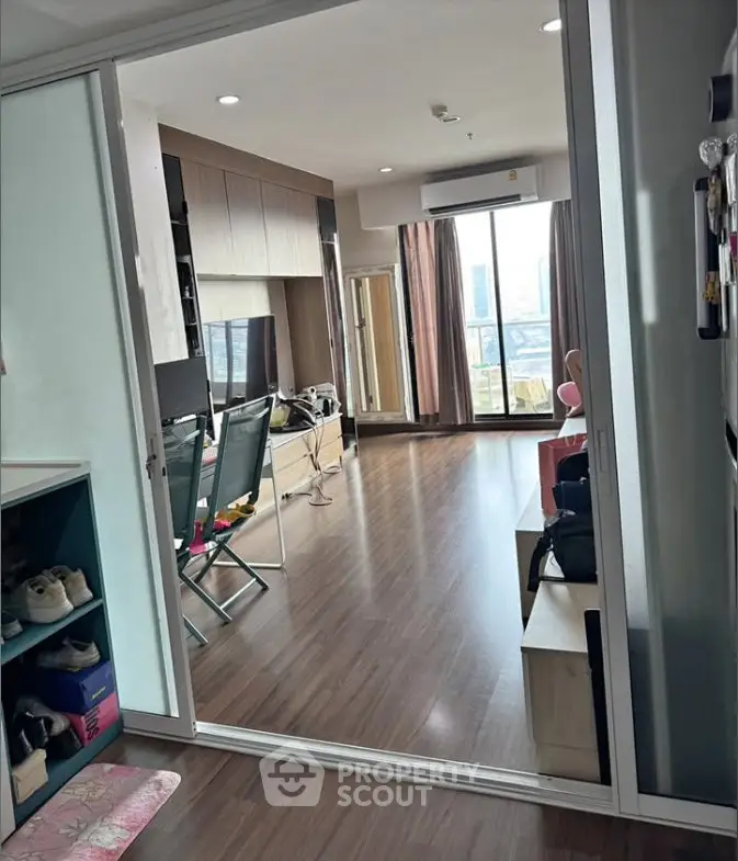 Spacious modern living room with wooden flooring and large windows offering city views.