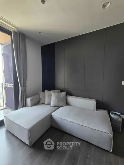 Modern living room with sleek gray sofa and floor-to-ceiling windows offering natural light.