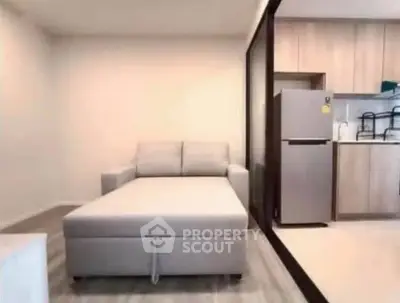 Modern studio apartment with cozy sofa and sleek kitchen featuring stainless steel fridge.