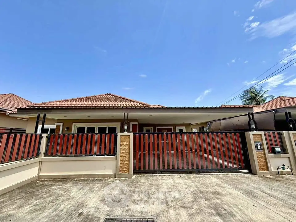 Charming single-story house with red fence and spacious driveway under clear blue sky.