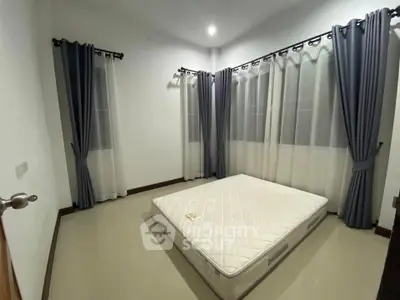Spacious bedroom with large windows and elegant curtains, featuring a comfortable mattress for a restful sleep.
