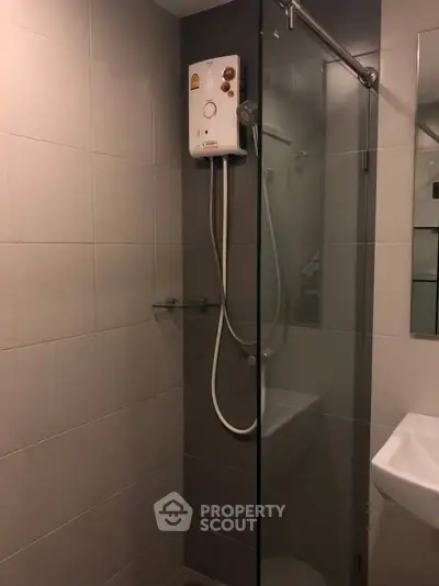 Modern bathroom with glass shower enclosure and water heater in sleek apartment.